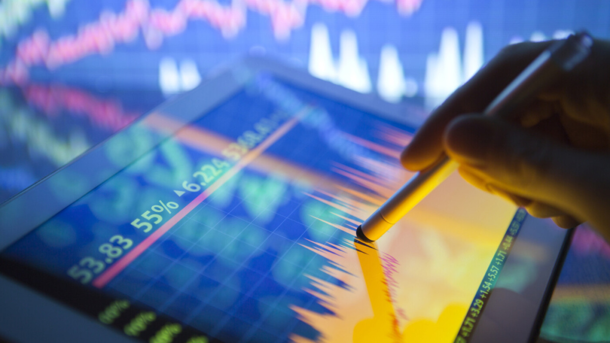 A hand using a digital tablet showing stock fluctuations